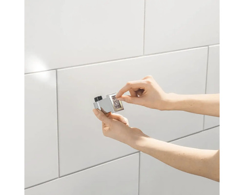 Osoba montuje chrómový prepínač na bielu obloženú stenu.