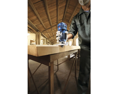 Osoba frézuje kus dreva hornou frézou Bosch