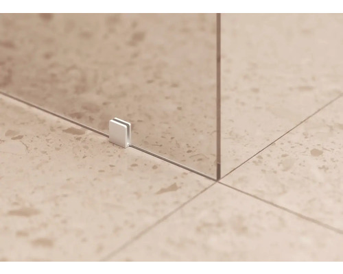 Detail sklenenej sprchovej steny s upevňovacou sponou na dláždenej podlahe.