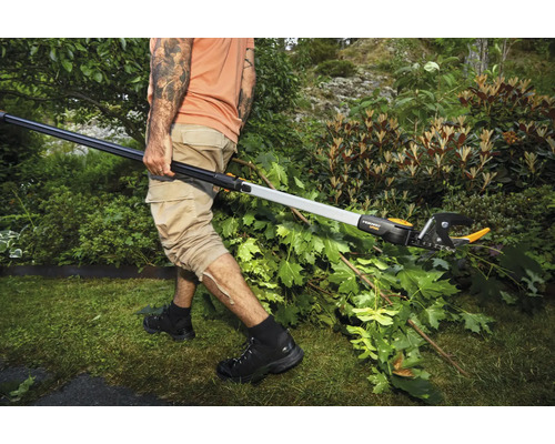 Osoba strihá konáre v záhrade pomocou teleskopických nožníc na konáre.
