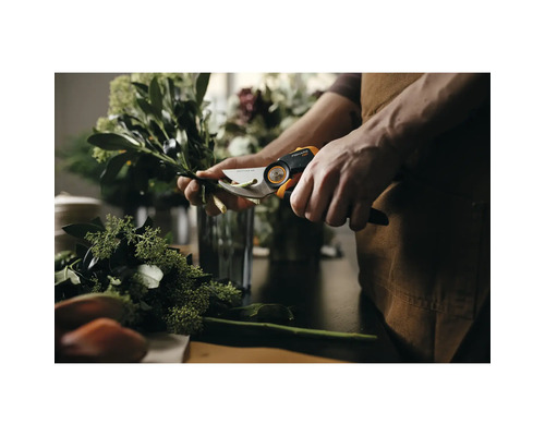 Osoba strihá konáre záhradnými nožnicami Fiskars na stole.