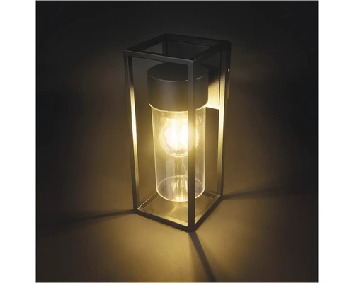 Čierne nástenné svietidlo s geometrickým kovovým rámom a valcovým skleneným difúzorom.