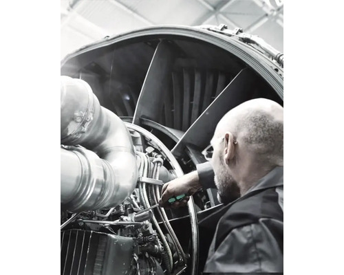 Muž kontroluje a udržiava motor lietadla pomocou skrutkovača.