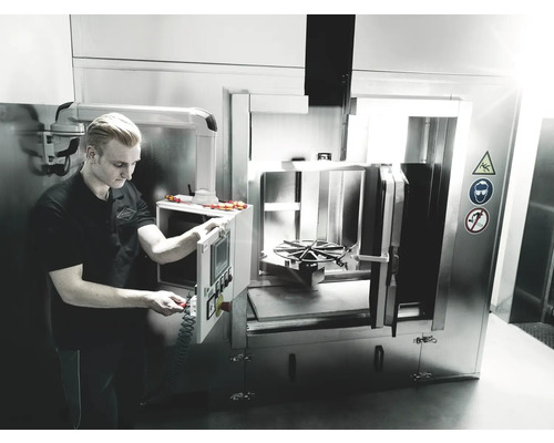 Zamestnanec obsluhuje oceľové čistiace zariadenie vo výrobnej hale.