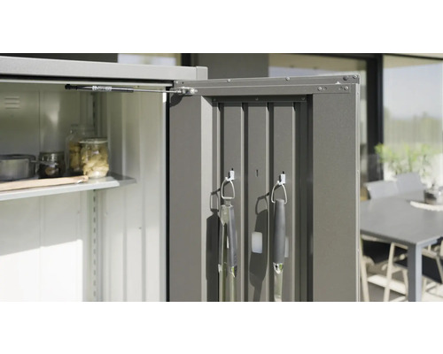 Otvorená kovová záhradná skriňa s policami a grilovacím náradím na vnútornej strane dverí