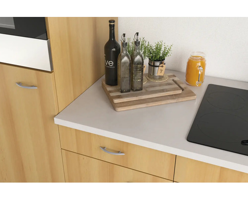 Kuchynská scéna s doskou na krájanie, fľašami oleja, bylinkami a varnou doskou na kuchynskej linke.