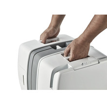 Dve ruky dvíhajú prenosnú mačaciu toaletu za držadlo.