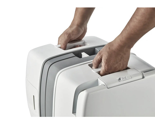 Dve ruky dvíhajú prenosnú mačaciu toaletu za držadlo.