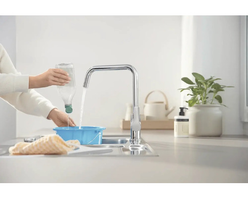 Osoba nalieva vodu z fľaše do modrej misky pod vodovodným kohútikom