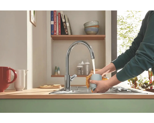 Kuchynská scéna s umývadlom, vodovodnou batériou a osobou umývajúcou šálku