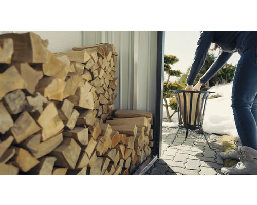 Sklad dreva s naskladaným palivovým drevom a ženou plniacou kôš drevom