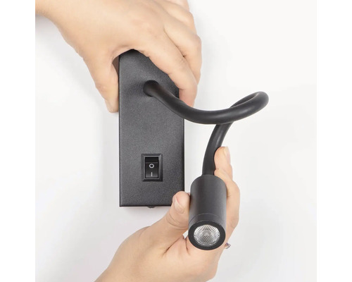 Osoba montuje čiernu čítaciu lampu s vypínačom na stenu.