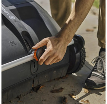 Osoba obsluhuje zametač trávnika s nastaviteľnou rukoväťou.