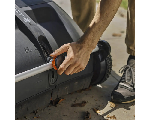 Osoba obsluhuje zametač trávnika s nastaviteľnou rukoväťou.