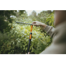 Záhradná scéna s osobou pripevňujúcou vejárové hrable k násade.