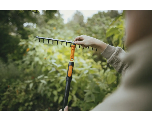 Záhradná scéna s osobou pripevňujúcou vejárové hrable k násade.