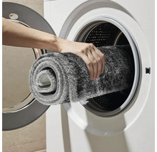 Osoba vkladá sivý kúpeľňový koberček do práčky.