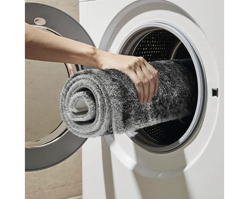 Osoba vkladá sivý kúpeľňový koberček do práčky.