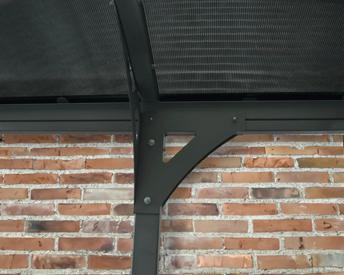 Detailný pohľad na záhradný pavilón s polykarbonátovou strechou a nosnou konštrukciou pri tehlovej stene