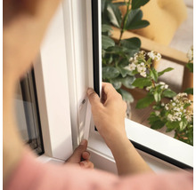 Osoba montuje okenné tesnenie na biely rám okna.