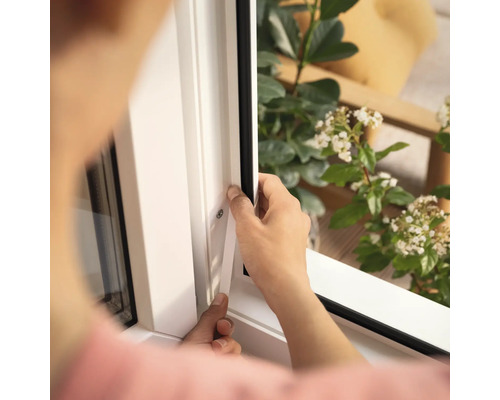 Osoba montuje okenné tesnenie na biely rám okna.