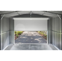 Vnútorný pohľad na kovový domček na náradie so stenami z vlnitého plechu a pootvorenou rolovacou bránou s výhľadom na dláždenú cestu.