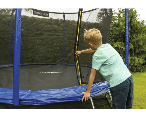 Dieťa otvára žltý zips na ochrannej sieti trampolíny Marimex s modrým krytom pružín v záhrade.