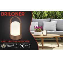 Briloner Logo, akumulátorová LED stolná lampa na drevenom stole v záhrade s pohovkou a plotom, teplá biela 3000 Kelvinov, krytie IP44.
