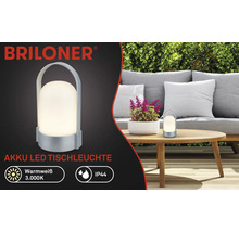 Logo Briloner, stolná LED lampa na akumulátor, teplá biela 3000 kelvinov, IP44, prenosná s rúčkou, na záhrade na drevenom stole.