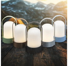 Päť prenosných outdoorových LED lámp v rôznych farbách na drevenom stole v daždi s horami v pozadí.