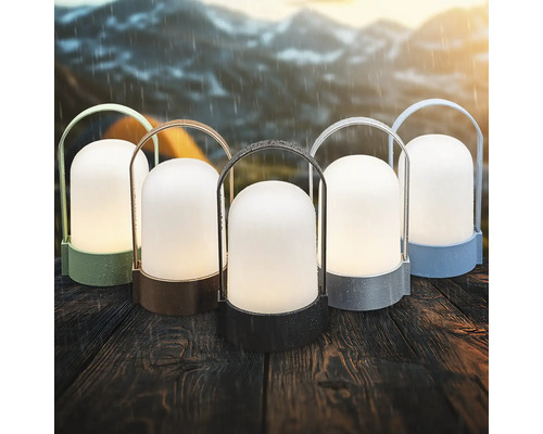 Päť prenosných outdoorových LED lámp v rôznych farbách na drevenom stole v daždi s horami v pozadí.