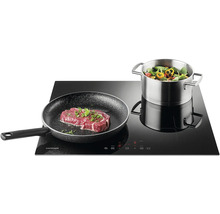 Indukčná varná doska Concept s panvicou so steakom a hrncom so zeleninou.