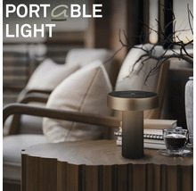 Moderná prenosná LED stolná lampa s valcovou základňou umiestnená na drevenom stole v útulnej obývacej izbe.