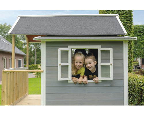 Dve deti vykúkajú z okna dreveného hracieho domčeka.