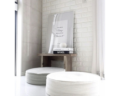 Scéna s dvoma okrúhlymi stoličkami, dreveným stolom a zarámovaným obrazom na tehlovej stene