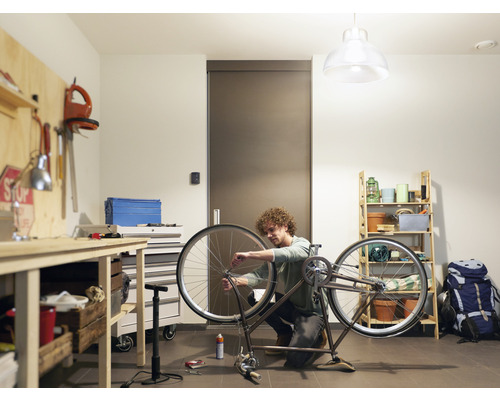 Muž opravuje bicykel v dielni s pracovným stolom a regálom