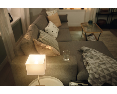 Obývacia izba so sivou rohovou sedačkou, vankúše, stolná lampa a príručný stolík