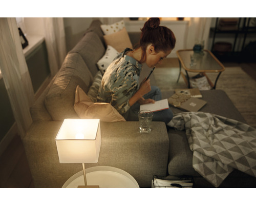 Žena sedí na pohovke a píše si poznámky vedľa stolnej lampy v obývacej izbe.