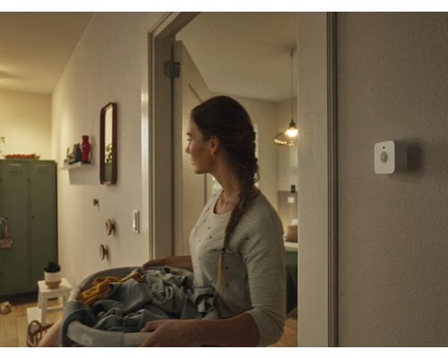 Žena s košom na bielizeň na chodbe s pohybovým senzorom na stene
