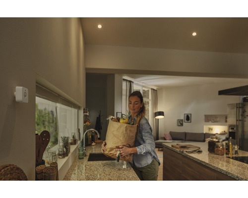 Žena s nákupnou taškou v kuchyni pod stropnými svietidlami a pohybovým senzorom.