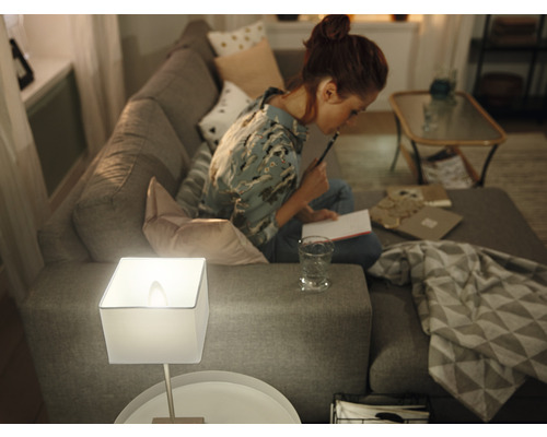 Obývacia izba s pohovkou, stolnou lampou a ženou sediacou na pohovke a píšucou.