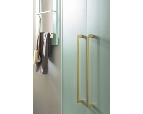 Detail kúpeľne so skrinkou s dvomi zlatými úchytkami a poličkou s uterákom a kefou.