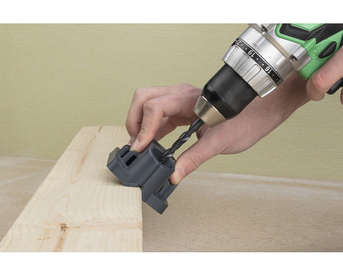 Vŕtačka s vrtákom vŕta do drevenej dosky pomocou vŕtacej šablóny.