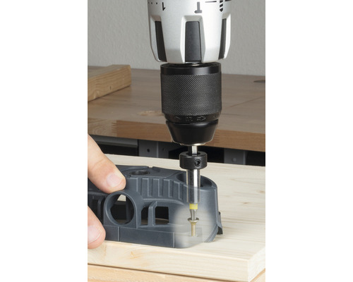 Vŕtačka s vŕtacím prípravkom vŕta otvor do drevenej dosky.