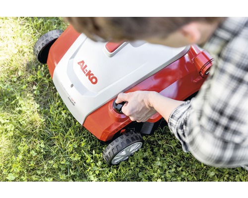 Osoba štartuje kosačku na trávu značky Al-ko na trávniku.