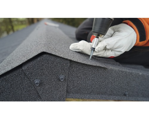 Remeselník pripevňuje strešné šindle na strechu pomocou akumulátorového skrutkovača.