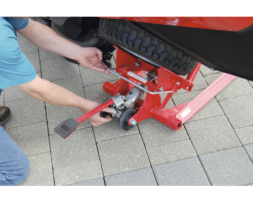 Osoba obsluhuje červený zdvihák na trávu pod traktorom na trávu.