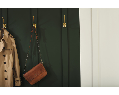 Scéna s trenčkotom a kabelkou zavesenou na zlatých nástenných háčikoch