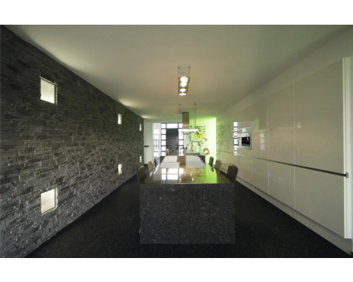 Svetlá miestnosť s kamennou dekoratívnou stenou, jedálenským stolom a kuchynskou linkou.