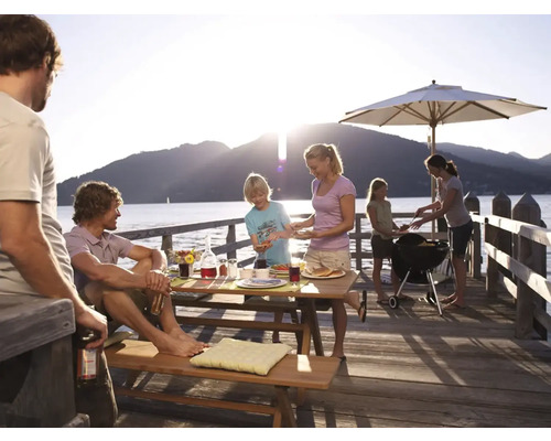 Rodina griluje na drevenom móle pri jazere s grilom, slnečníkom a piknikovým stolom